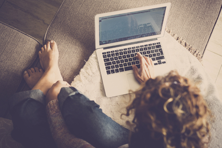 caucasian woman in casual clothes at home, barefoot and comfortable, type on a laptop working free and independent - alternative digitla nomad and frelance work style - viewed from aboveの写真素材