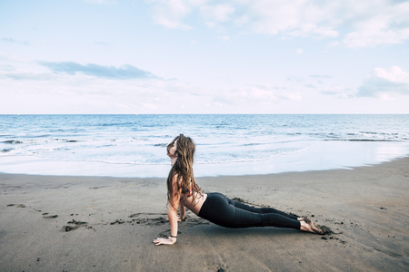 Plank fitness hard position at the beach with beautiful brunette girl enjoying a helthy sport fitness lifestyle outdoor - blue ocean horizon in background for summer exercises conceptの写真素材