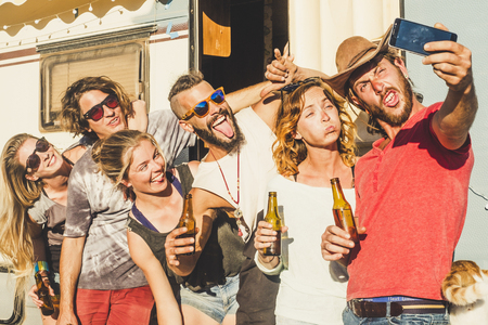 Group of crazy young caucasian people men and women taking selfie pictures doing funny expressions - friendship and youthful concept - old caravan in background and summer seasonの写真素材