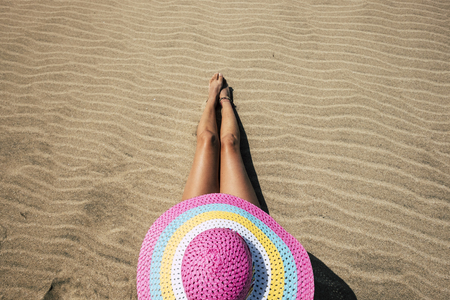 Vertical top view of summer concept beautiful legs and skin caucasian girl with pink hat having a sun bath at the sandy beach during vacation - colors and pattern concept with cute woman - nudism activityの写真素材