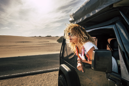 Beautiful lady caucasian people female enjoy th ewind in the outdoor nature out of her black car - desert outdoor around and alternative vacation journey concept for cute young adultの写真素材