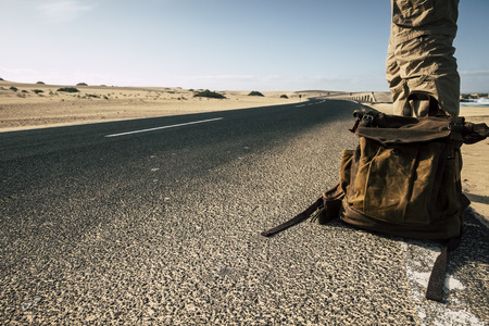 Close up ground point of view of man with leather backpack travel and wait for a car to share the trip together - sand and desert dunes and black asphalt road for traveler people enjoying lifestyleの写真素材