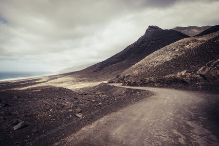 Off road adventure road in the mountains with beach view in wild scenic landscape for alternative travel vacation in the outdoors - cloudy dramatic sky for freedom holiday conceptの写真素材