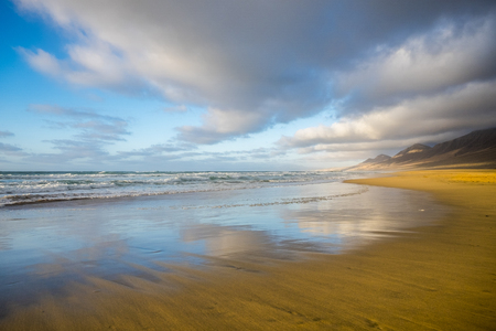 Lonely beach coloured and reflected with beautiful mountain background  with cloudy sky - summer tropical vacation concept in free sandy scenic place with nobody thereの写真素材