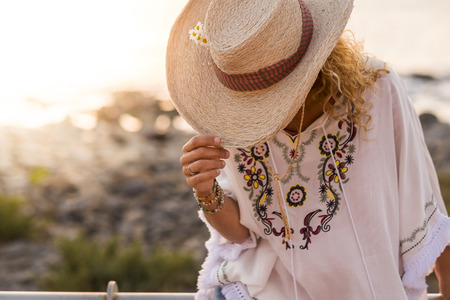 Fashion style clothes and unrecognizable caucasian woman hidden by cowboy vacation hat - travel and holiday summer concept with defocused beach background in sunny dayの写真素材