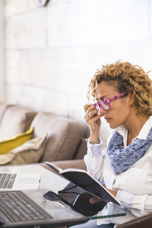 Beautiful caucasian young woman at home work or study with two personal laptop on the desk - people studying over 40 years of age concept - business woman free from officeの写真素材
