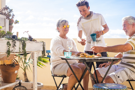 grandfathers adult mature and teenager nephew enjoy outdoor in the terrace some leisure with food and drinks. ocean and city view, vacation sunny day nice weather concept and background. happy people family togetherの写真素材