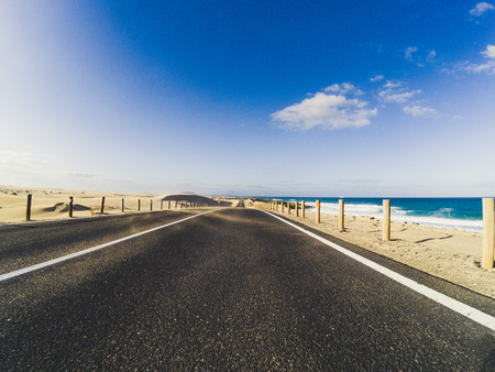 Long way road for travel car transportation concept with desert and beach on the side - sea water and blue clear beautiful sky in background - motion effectの写真素材