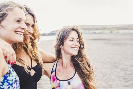 Cheerful caucasian girls together in friendship at the beach enjoying vacation and outdoor leisure activity together - smiling attractive young women friends - clear white sky backgroundの写真素材