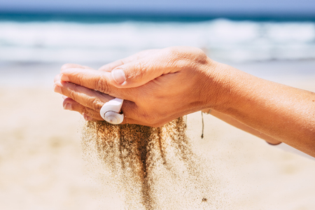 Environment and respect for the nature with close up of woman hands taking sand falling down - beach and blue sky ocean water in background - summer holiday vacation conceptの写真素材