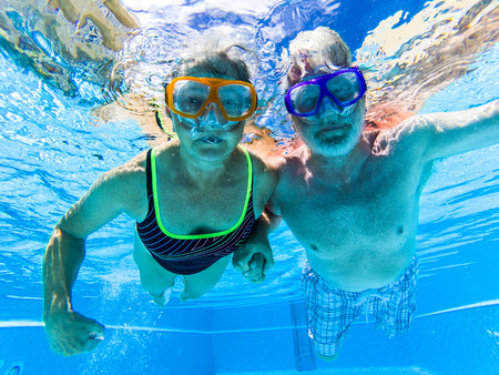 Adult people senior couple have fun swimmin in the pool underwater with coloured funny diving masks - dive concept and active retired man and woman enjoying the lifestyle - blue water and caucasian adultsの写真素材