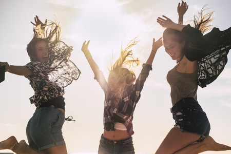 Youthful people beautiful young girl jumping and celebrating for happiness outdoor with sun in backlight - have lot of fun and laugh together in friendship - happy lifestyle conceptの写真素材