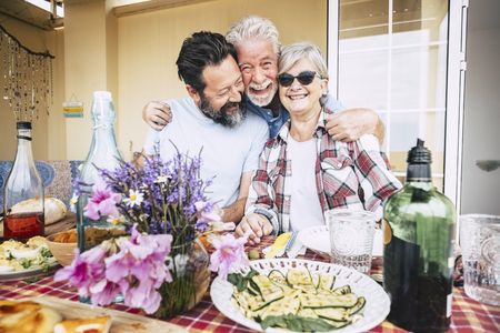 Happy family people aged senior adult portrait hugging and having fun in front of a table full of food and beverages ready to celebrate all together in friendship and happinessの写真素材