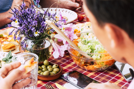 Close up with people friends eating and having fun together having lunch on a table full of food - coloured tasty vegetables and more - seasonal flowers in the middle -の写真素材