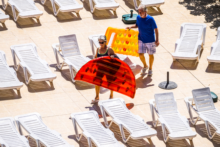 People in summer time with adult senior caucasian coiple with coloured trendy lilos approaching to the swiming pool to have some fun and relax on summer outdoor leisure activity togetherの写真素材