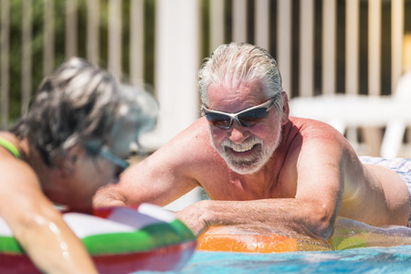 Cheerful happy smiling people senior man enjoying the summer swimming pool in couple retired nice lifestyle - white hair and summer holiday vacation or relax leisure activityの写真素材