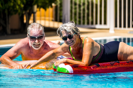 Happy joy cheerful people adult senior couple have fun in the swimming pool with trendy coloured lilos mattress on a blue water in hotel resort for summer holiday vacation lifestyleの写真素材