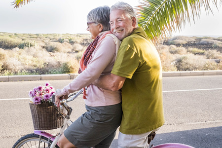 beautiful aged couple of senior in vacation go both on an old bike and enjoy the summer sunlight. tropical place and country side desert in background - concept or friendship and relationship for maturesの写真素材