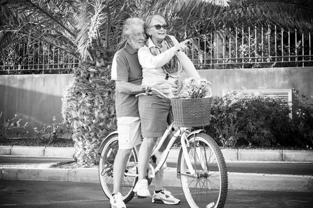 Black and white picture couple man and woman senior mature people enjoying and have fun riding both the same old vintage bike together - forever together in happiness lifeの写真素材