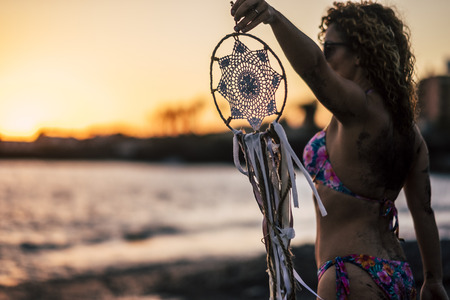 Beautiful people woman with bikini holding a white dreamcatcher outdoor at the beach enjoying sunset in a summer holiday vacation freedom feelingの写真素材