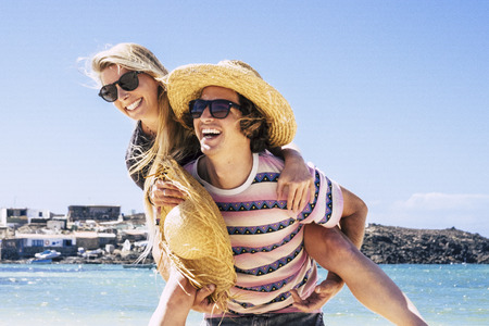 Young caucasian couple having fun at the beach in summer holiday vacation tourist people love travel and live together - happy lifestyle for man carrying laughing woman on his back - blue sky and sea in backgroundの写真素材