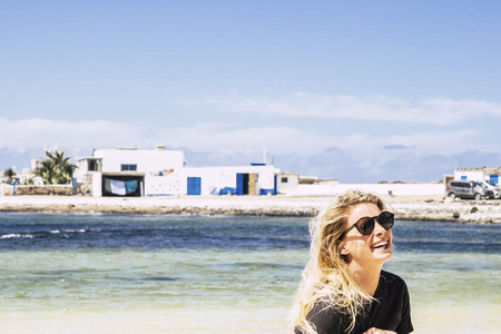 Real life beautiful blonde girl laughing a lot outdoor - traditional town on the coast line and blue wonderful sea in background - clear sky and colors for happiness and joyful conceptの写真素材