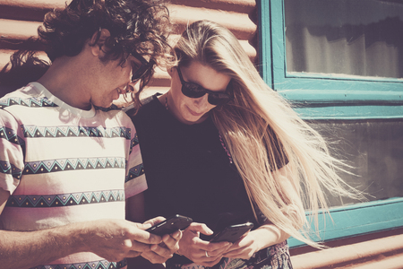 Young beautiful people couple enjoyimg and using modern cellular phone together looking the devices and enjoying the internet connection - vintage colors filter style for millennialの写真素材