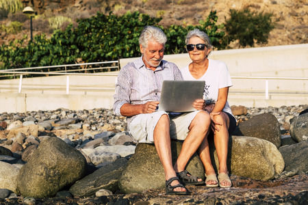 adult senior aged couple cacuasian people use technology laptop computer outdoor in a sunny day - internet everywhere and retired man and woman with notebook sitting on the rocks in outdoorの写真素材