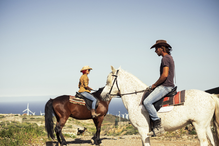 Happy caucasian couple of riders with horses. Outdoor, windmill in the background. Horizon over waterの写真素材