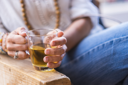 Close up of woman with coloured fashion accessories and jeans taking holding a glass of healthy tea for afternoon break time - beverage and relaxing activityの写真素材