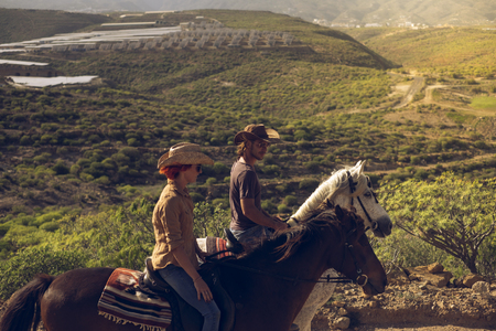 Young people in outdoor leisure activity together in couple enjoying a riding on her horse brown and white on a beautiful mountain valley - people with animals concept of alternative lifestyleの写真素材