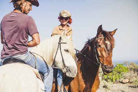 Happy smiling couple doing a horse riding togethe rin the nature - outdoor leisure activity for young people together in friendship with animals for therapyの写真素材