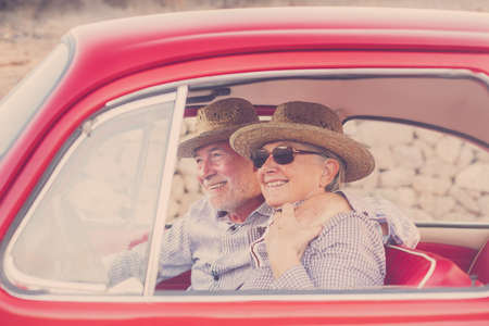 nice adult couple hug and love inside a red old vintage car parked on the road. smiles and have fun traveling together. happiness and lifestyle for nice people. summer time and vacation journeyの写真素材