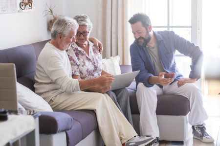 Adult and senior family at home with parents and son - caucasian people sitting on the sofa working with technology devices laptop and phone together enjoying internet connectionの写真素材