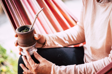 Close up coloured image with old senior hands woman caucasian drinking a natural tea from a wooden cup - natural healthy lifestyle for alternative peopleの写真素材