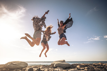 Group of young people celebrating and having fun together in friendship jumping at the beach with ocean and sunset in background - summer holiday vacation conceptの写真素材