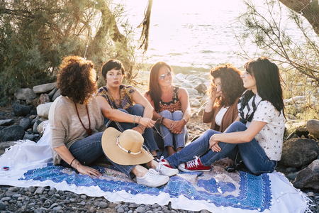Group of young adult caucasian people women sit down in outdoor leisure activity together at the beach enjoying the sunset light in friendship - friends in beautiful place conceptの写真素材