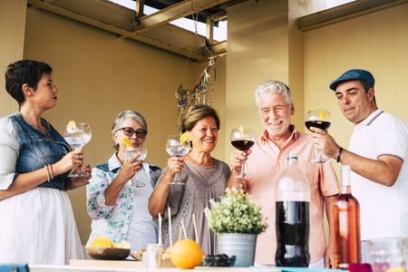 Group of mixed ages caucasian people enjoy together the lunch outdoor at home with big glass of wine and cocktail - family and friendship concept with cheerful men and womenの写真素材