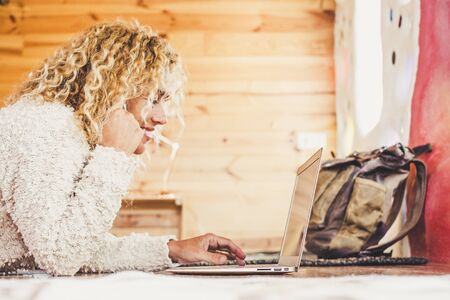 Cheerful happy beautiful blonde curly caucasian woman working at computer laptop lay down onthe floor at home or hotel for travel vacation - alternative office for free job - freelance and travel conceptsの写真素材