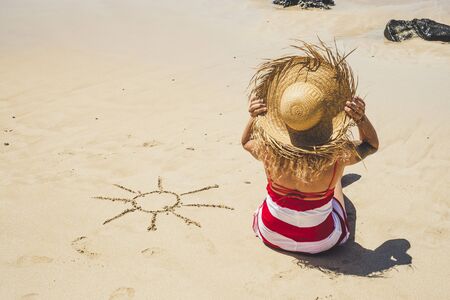 Summer holiday vacation at the beach in paradise beautiful resort people concept with nice woman with tourist hat viewed from back enjoying the sand and with sun designed on her sideの写真素材