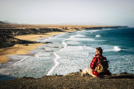 Wanderlust and travel people concept with hipster man sitting on the rocks at the cliff with wonderful beautiful view on a natural undiscovered beach - enjoy nature outdoorの写真素材