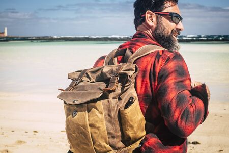 Travel and backpack wanderlust concept people with adult hipster man with beard and sunglasses enjoying the outdoor leisure activity with beach and beautiful sea in backgroundの写真素材