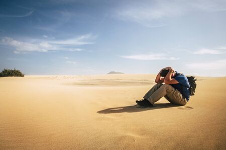 Lonely depserate adventure backpacker man sit down alone nowhere in the desert dunes - arid climate change concept for people travel the beautiful world - extreme trekking vacationの写真素材