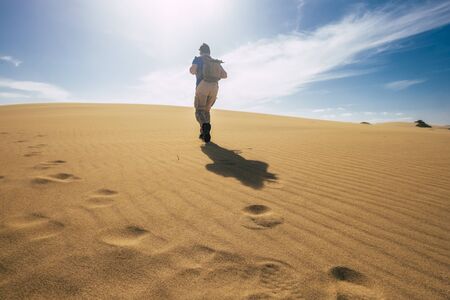 Backpacker people explore and adventure leisure activity concept with man walking on the desert dunes with backpack - alternative vacation for freedom lifestyle - scenic nature outdoorの写真素材