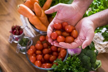 Vegetables for vegetarian or vegan or healthy food lifestyle people - mixed of colors and vitamins on the table ready to be eaten for weight loss and health - caucasian man taking cherry tomatoesの写真素材
