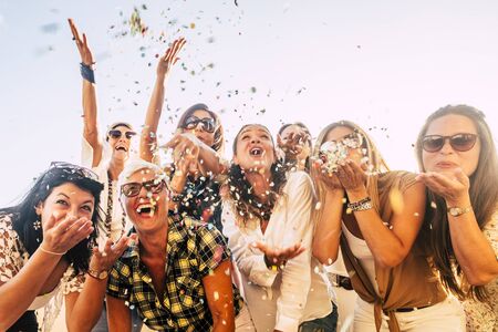People having fun in party celebration friends concept - group of young and adult women all together laughing blowing coloured confetti - friendship and love for lifestyle with mixed active generationsの写真素材