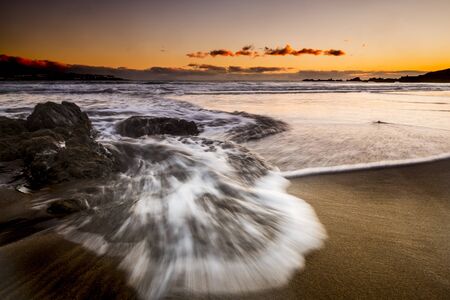 Long exposure sea beach sunset landscape with wave and coloured sunset with orange sky - beauty of the nature and timeless vacation in tropical ocean scenic place conceptの写真素材