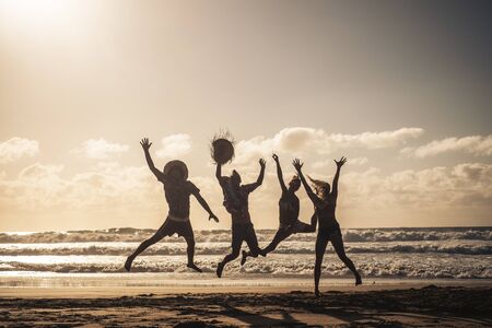 Group of people jump happy together at the beach during sunset with sky in background and silhouette bodies - summer vacation holiday for friends people have fun in outdoor leisure activityの写真素材