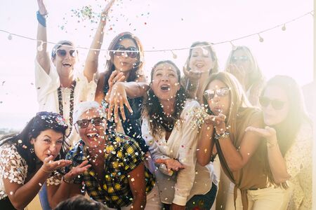 Group of people celebrate together having a lot of fun blowing coloured confetti - friendship and diversity ages generation laugh and smile on party - cheerful joyful concept for ladiesの写真素材
