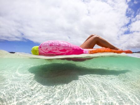 Underwater view of nice caucasian woman enjoying the summer holiday vacation relaxing on a coloured trendy lilo in the transparent caribe sea - people having sunbath at tropical beachの写真素材